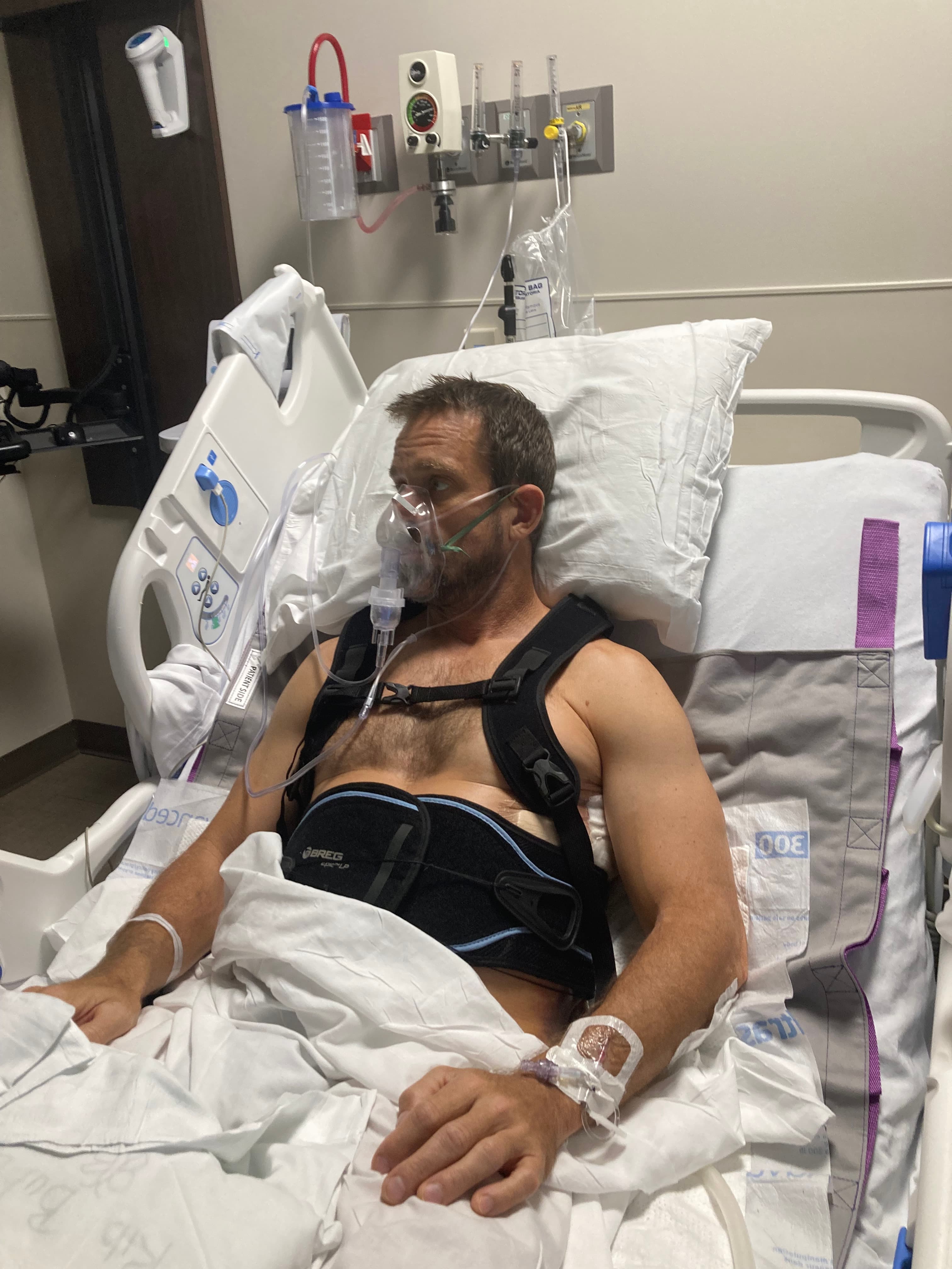 Michael Cavett recovering in a hospital bed with a brace and mask