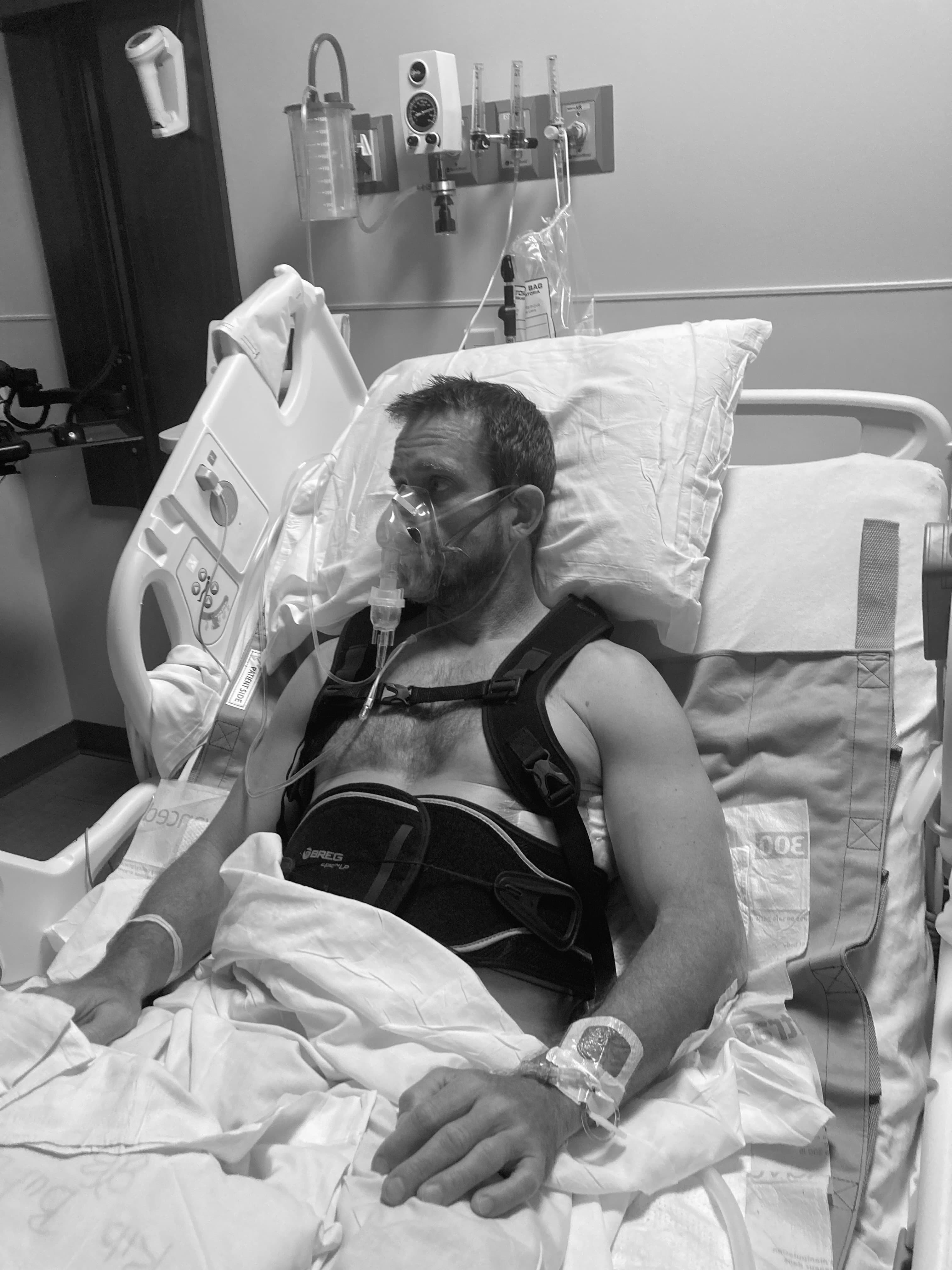 Michael Cavett recovering in a hospital bed with a brace and mask