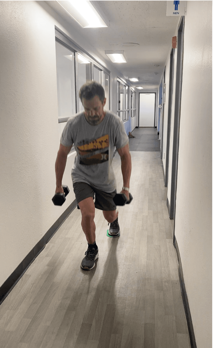 Michael Cavett doing a sliding lunge with dumbbells in a hallway